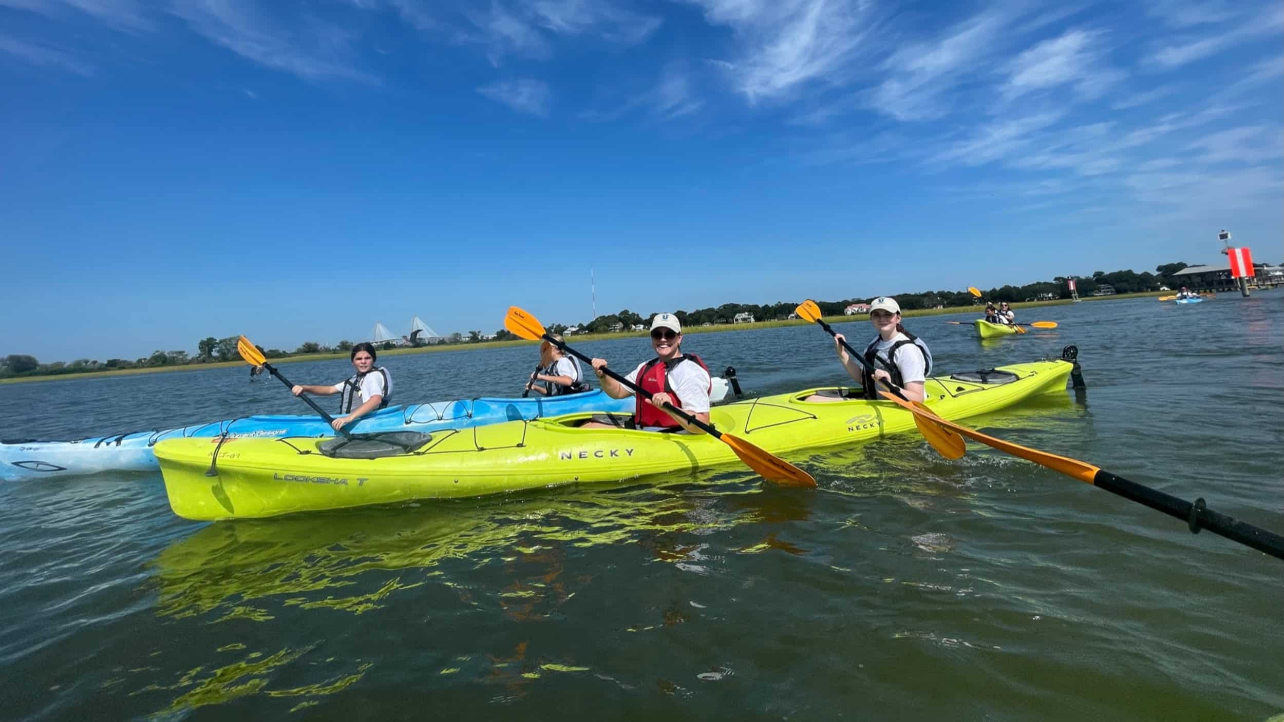 A trio of USL students with an adult chaperone smile with kayaking along a coastal waterway