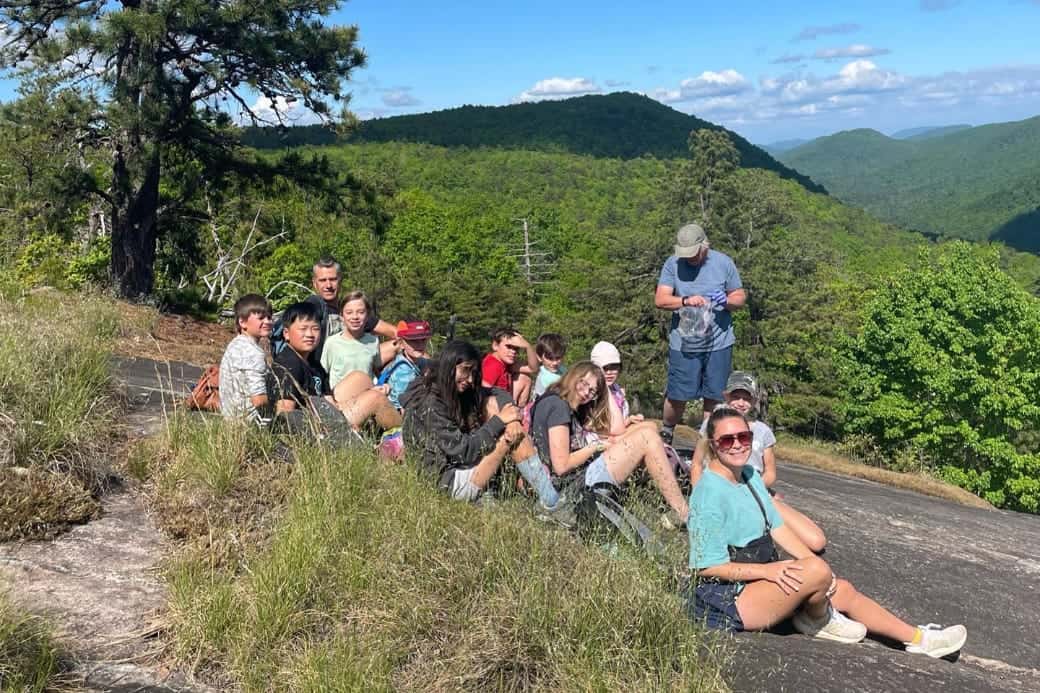 A group of students and adult chaperones pause outdoors with mountains in the background