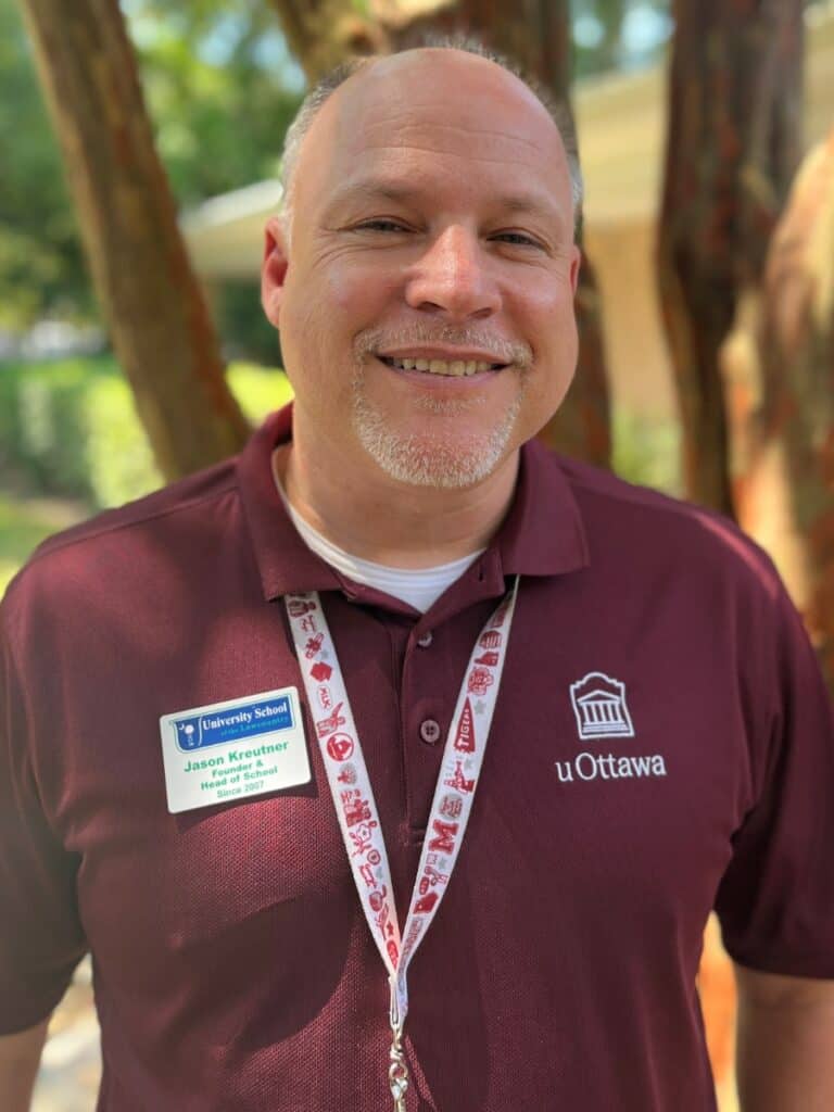A smiling man, Jason Kreutner, wearing a lanyard and a name tag, pictured outdoors, looking at the camera
