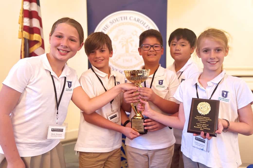 A smiling group of students grip a trophy cup and a plaque