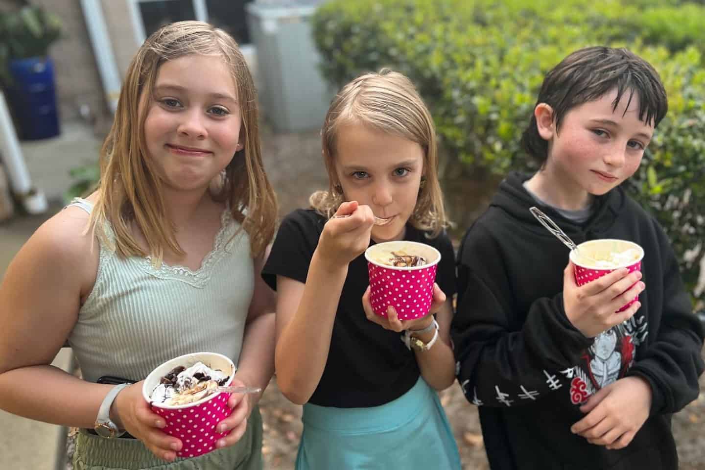 A smiling trio of students enjoy ice cream sundaes outdoors
